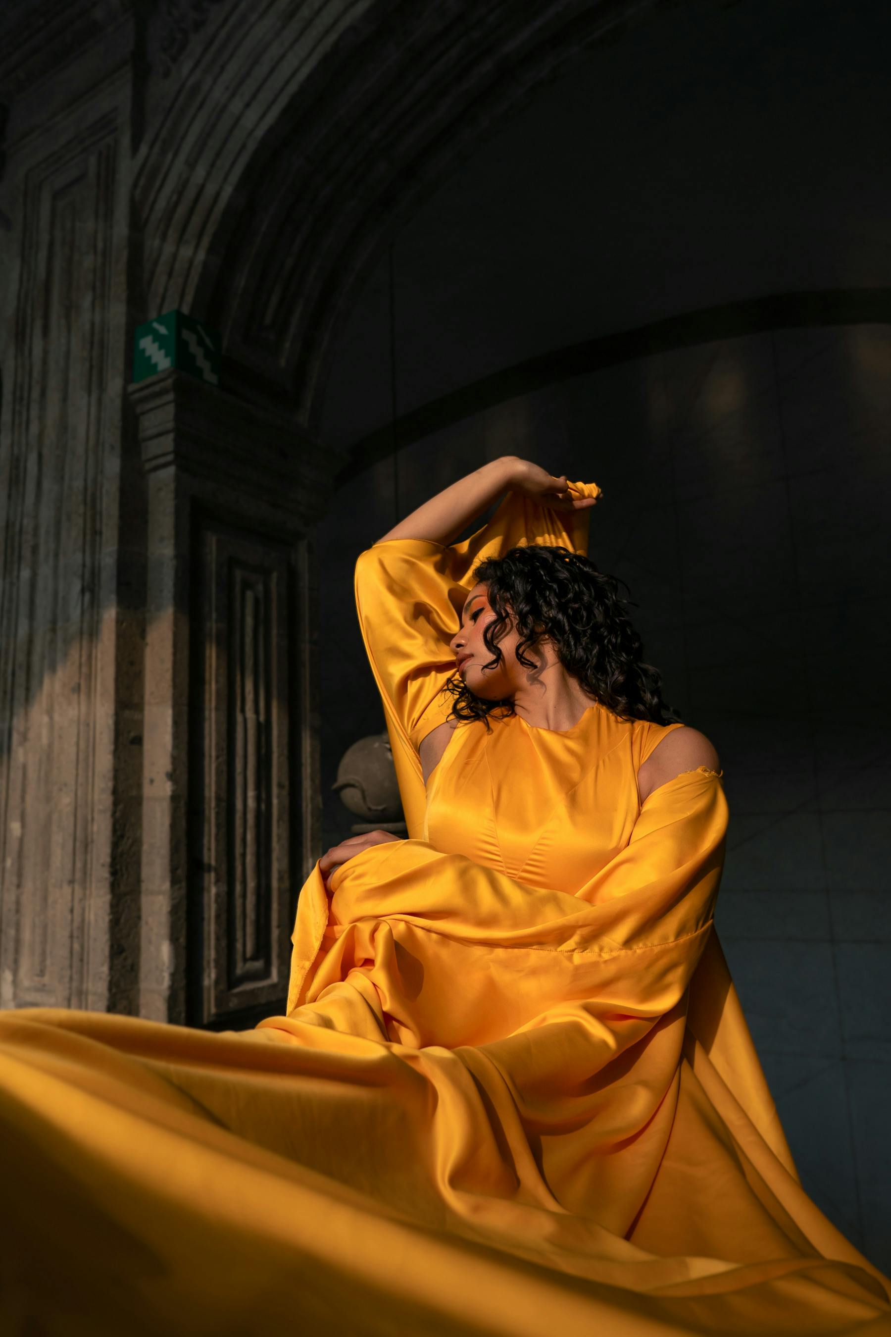Captivating fashion portrait of a woman in a flowing yellow dress, highlighting light and shadow within historical architecture.