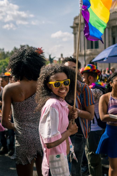 Free Joyful people celebrating at a vibrant pride parade, waving a colorful rainbow flag outdoors under a sunny sky. Stock Photo