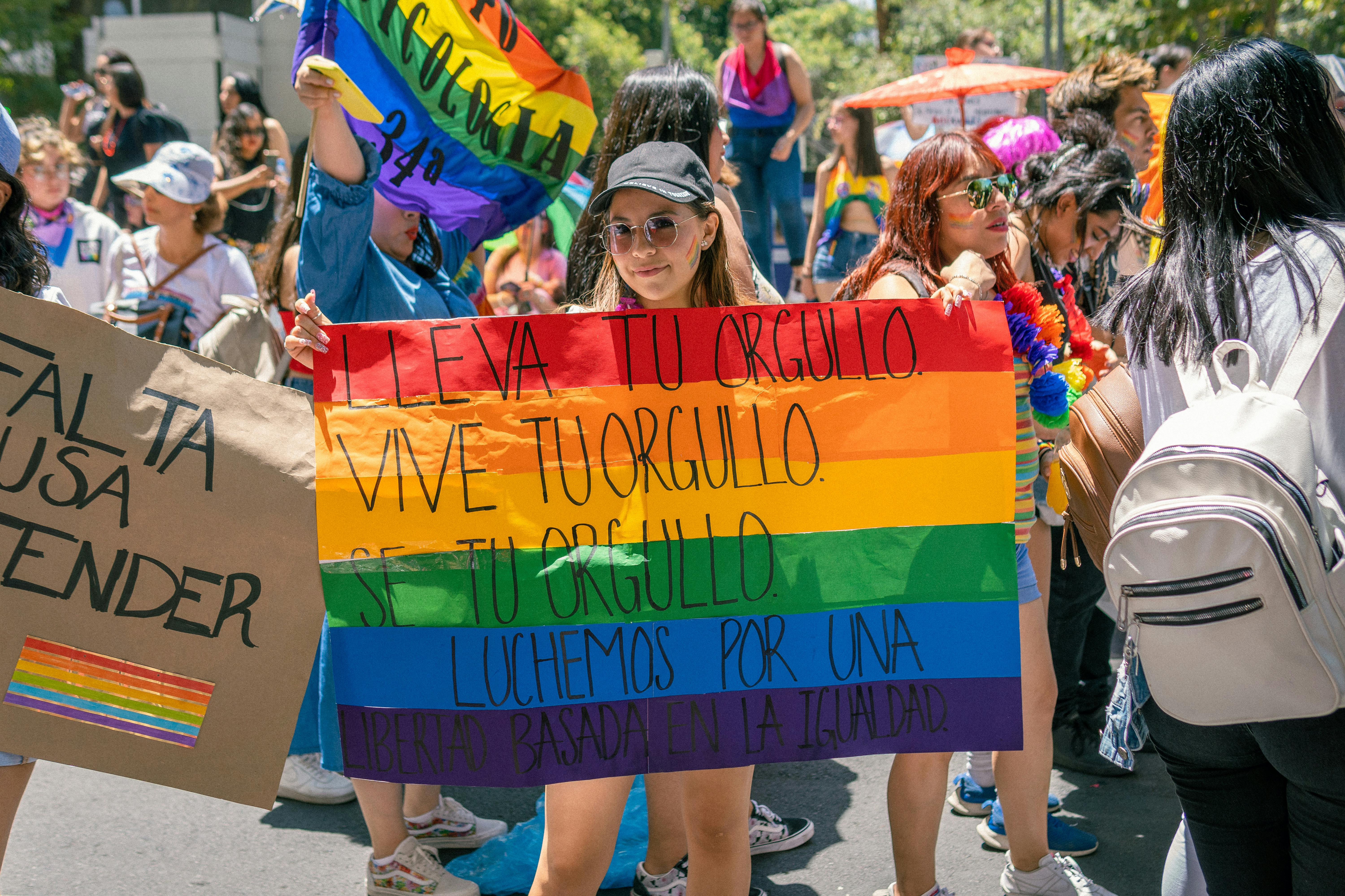 Colorful LGBTQ pride parade with participants holding rainbow flags and signs advocating equality.
