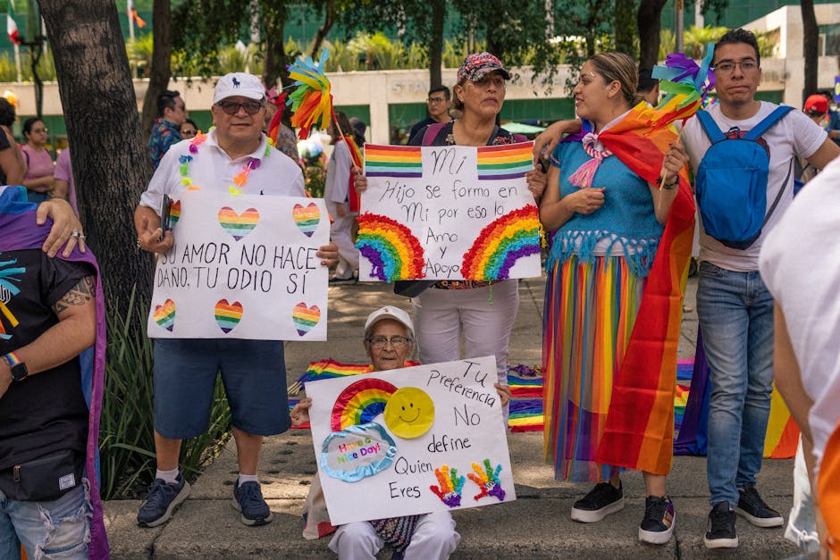 Colorful LGBTQ gathering with supportive signs and flags at daytime outdoor event.