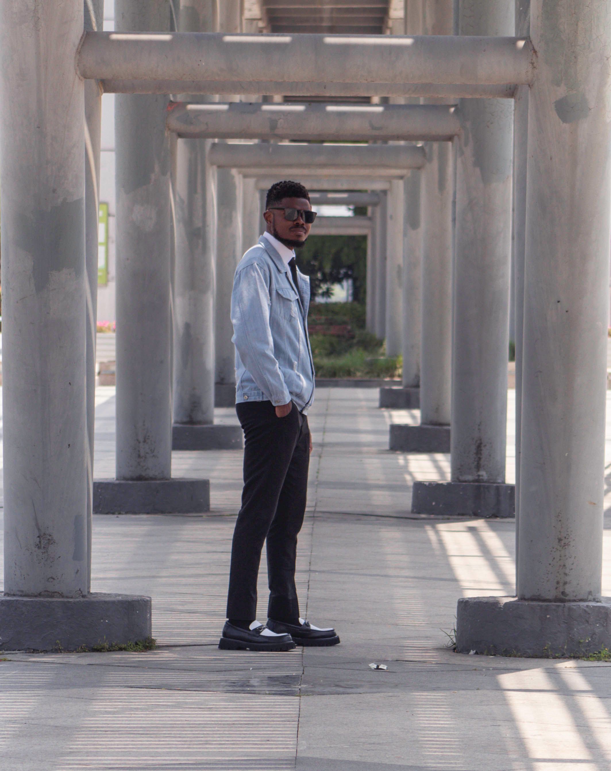 Casual man standing under a geometric structure in a city setting.