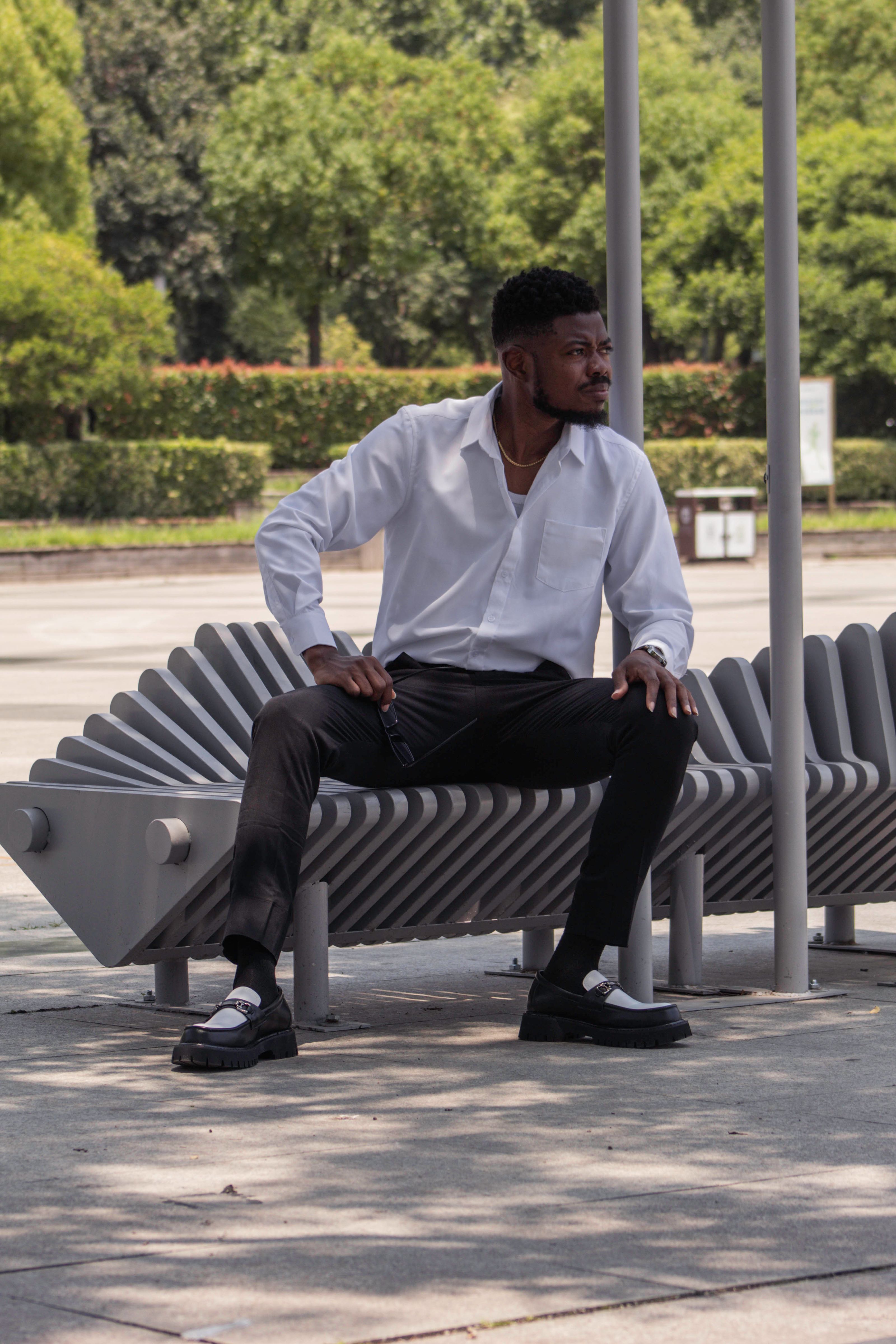 Homem em traje casual elegante sentado em um banco moderno ao ar livre em um dia ensolarado.