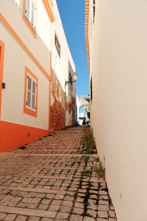 Free A picturesque cobblestone alleyway between colorful buildings in Algarve, Portugal, on a sunny day. Stock Photo