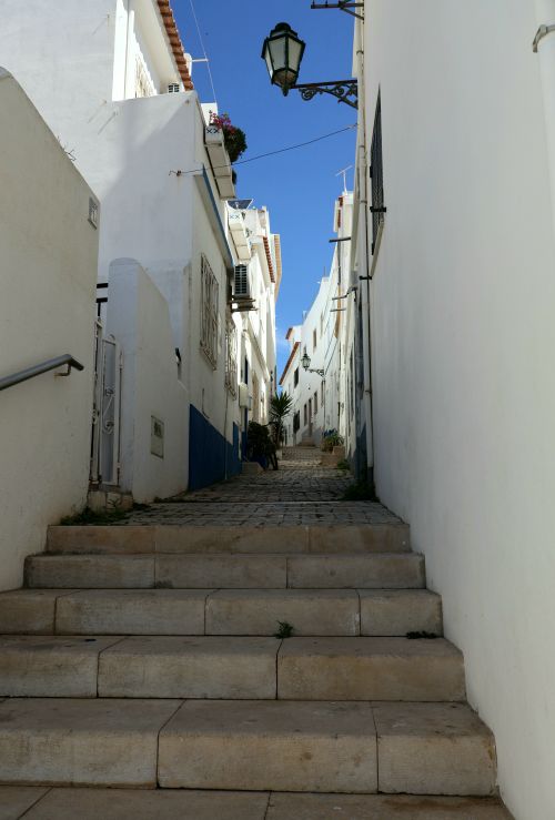 Free Narrow stone alley lined with whitewashed buildings under a clear blue sky. Stock Photo
