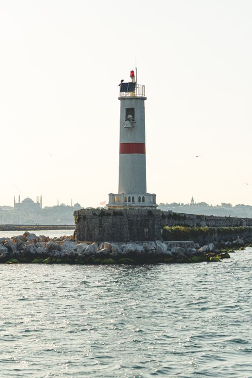 Free A tall lighthouse stands on a rocky coastline surrounded by calm waters. Stock Photo