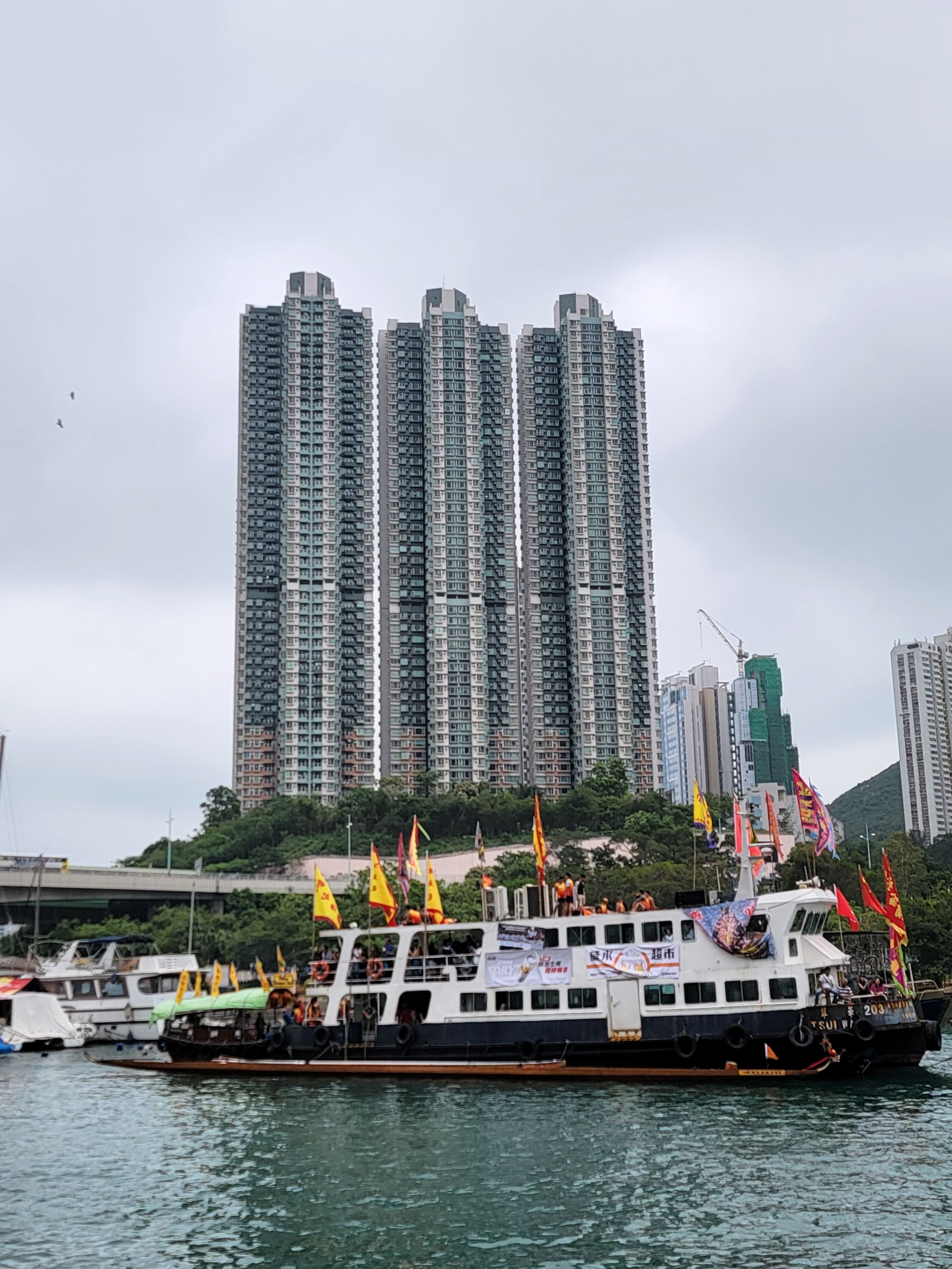 A dragon boat festival scene with a lively boat near tall Hong Kong skyscrapers.