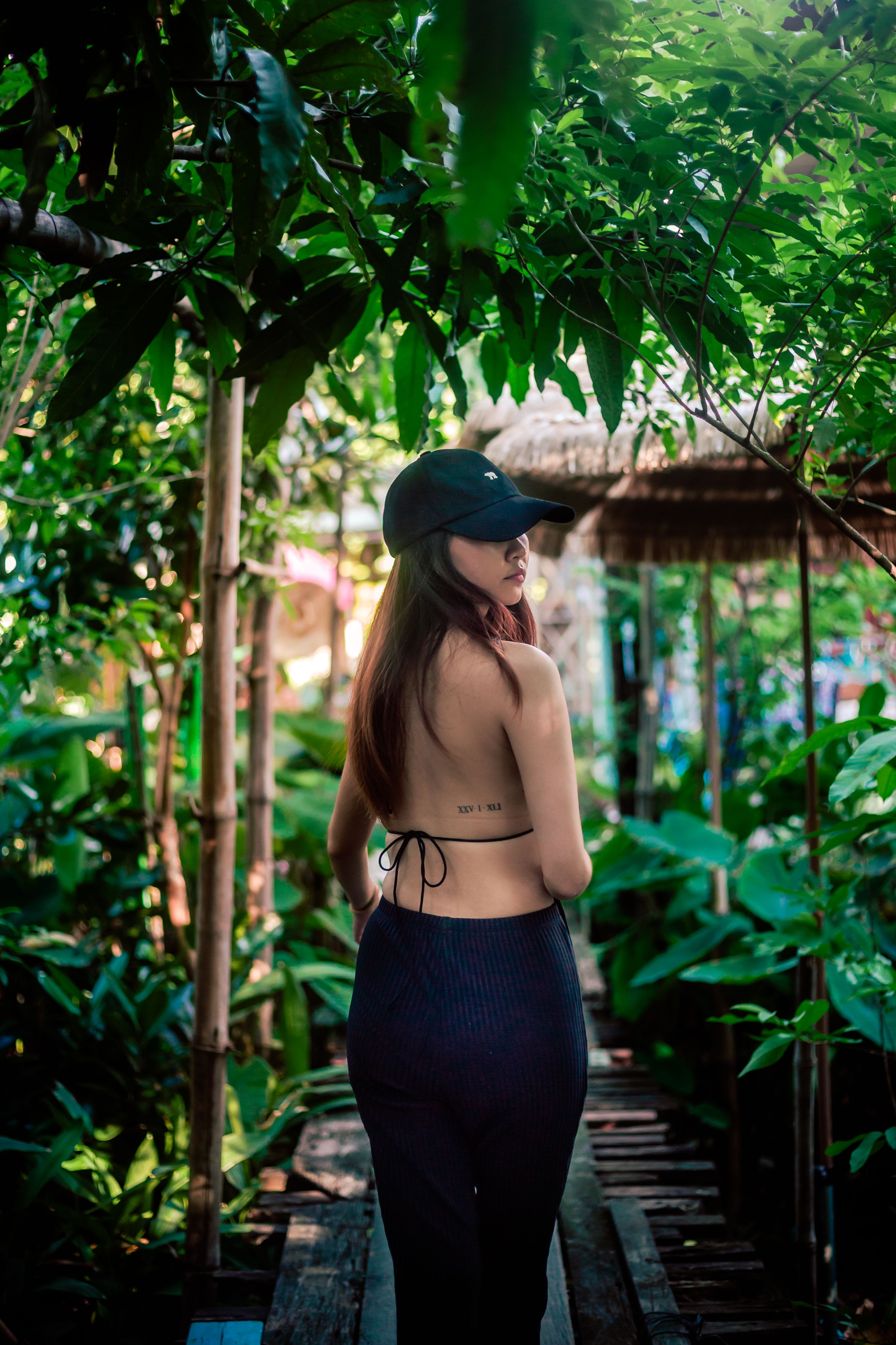 Model in casual summer attire strolling along a lush jungle path under sunlight.