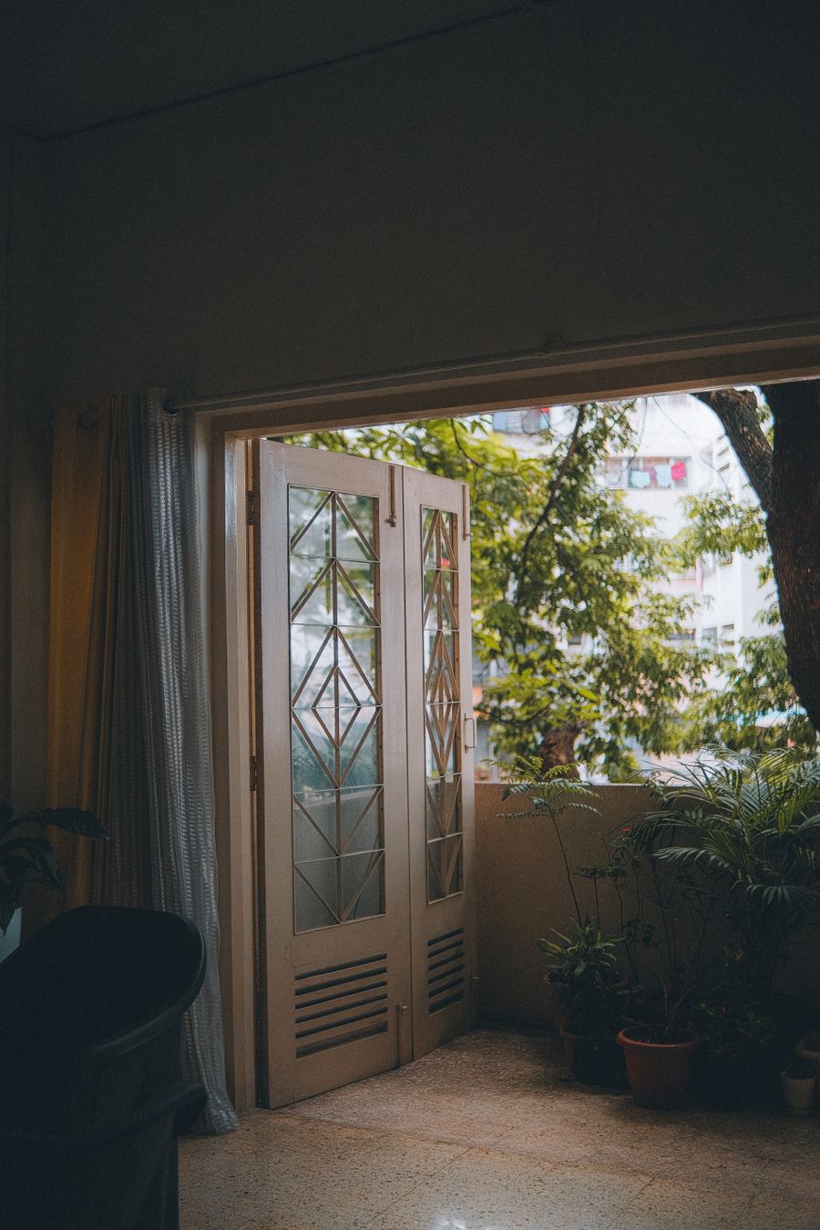 Puertas de cristal abiertas desde el interior de un departamento hacia un balcón lleno de plantas