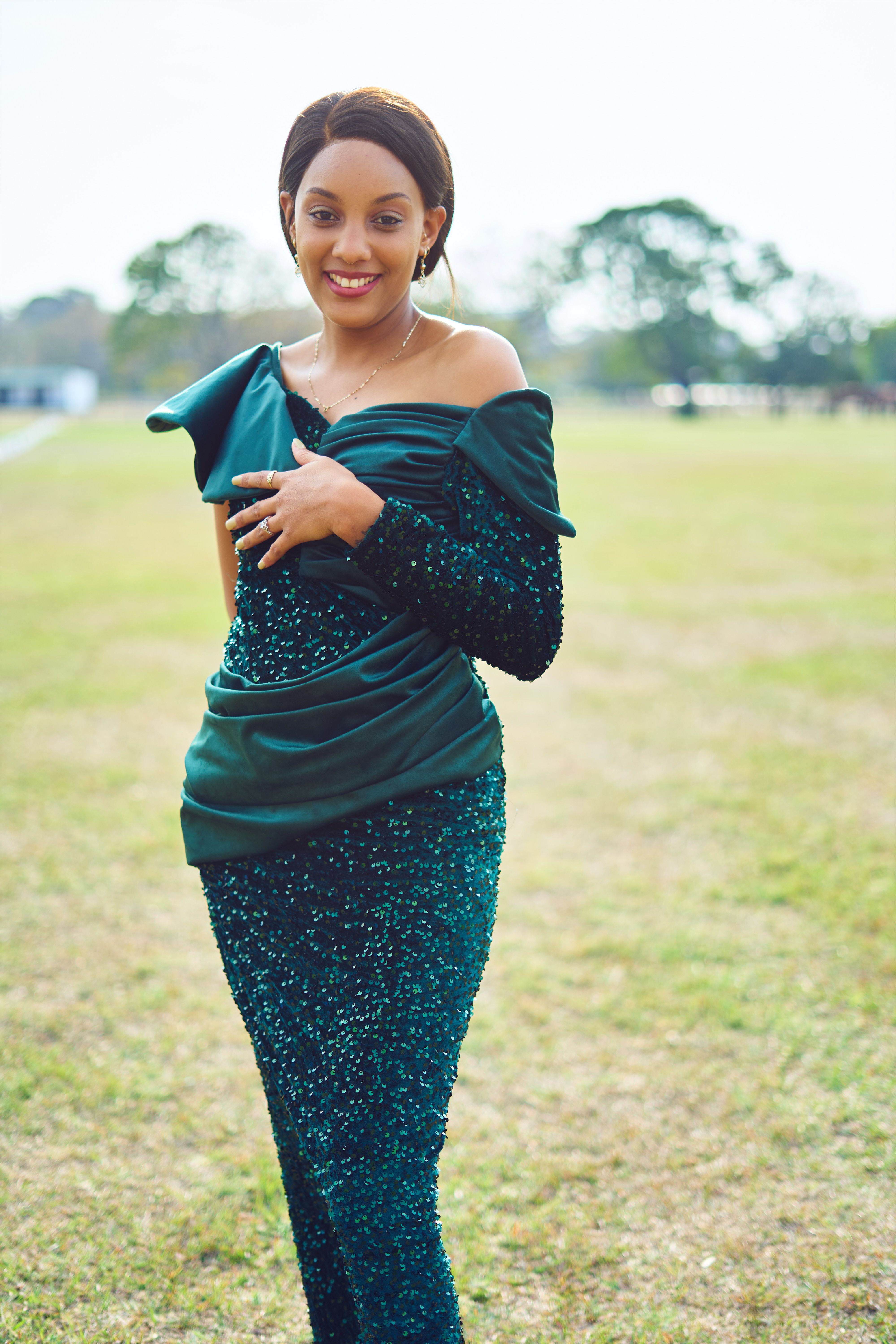 A woman in an elegant emerald green dress smiles in an outdoor setting, exuding confidence and charm.