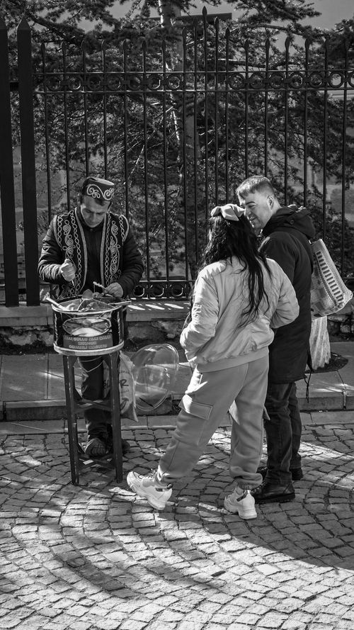 Free Black and white image of a street vendor selling goods to two adults on a cobblestone path. Stock Photo