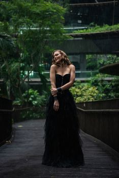 Woman in a black dress posing outdoors in a lush, rainy setting. Dramatic and elegant aesthetic.