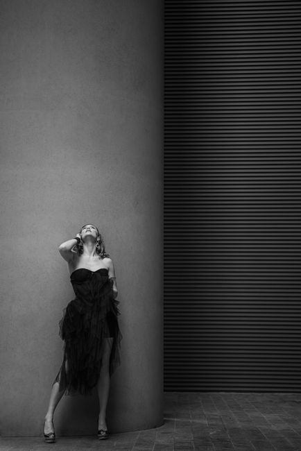 Black and white photo of woman in black dress leaning on modern building column.