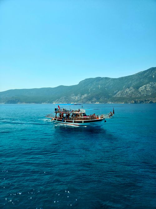 Free A boat with passengers navigates the clear blue waters off Antalya, Türkiye, with a mountainous backdrop. Stock Photo