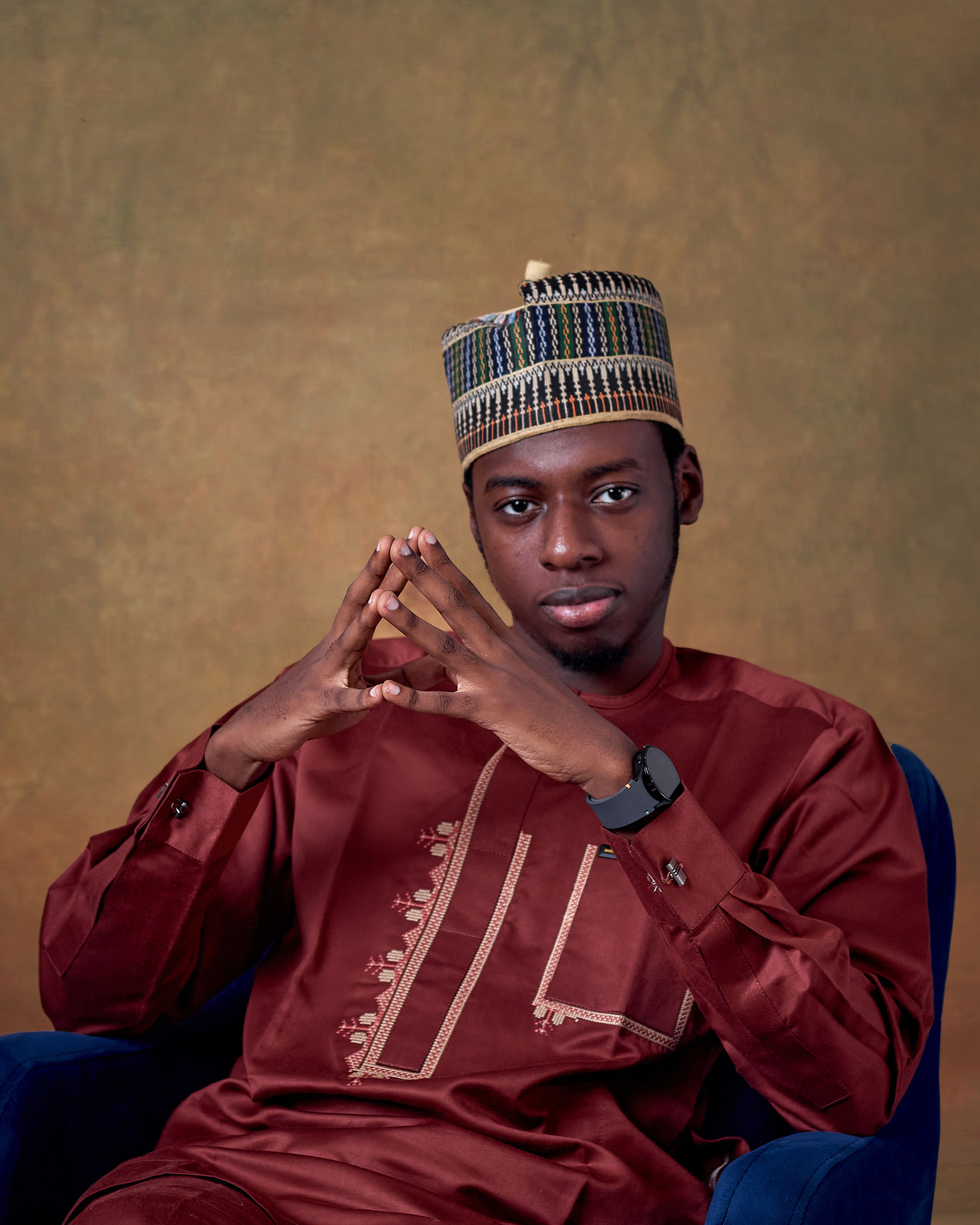 Elegant portrait of a man in traditional attire with confident pose, against a warm backdrop.