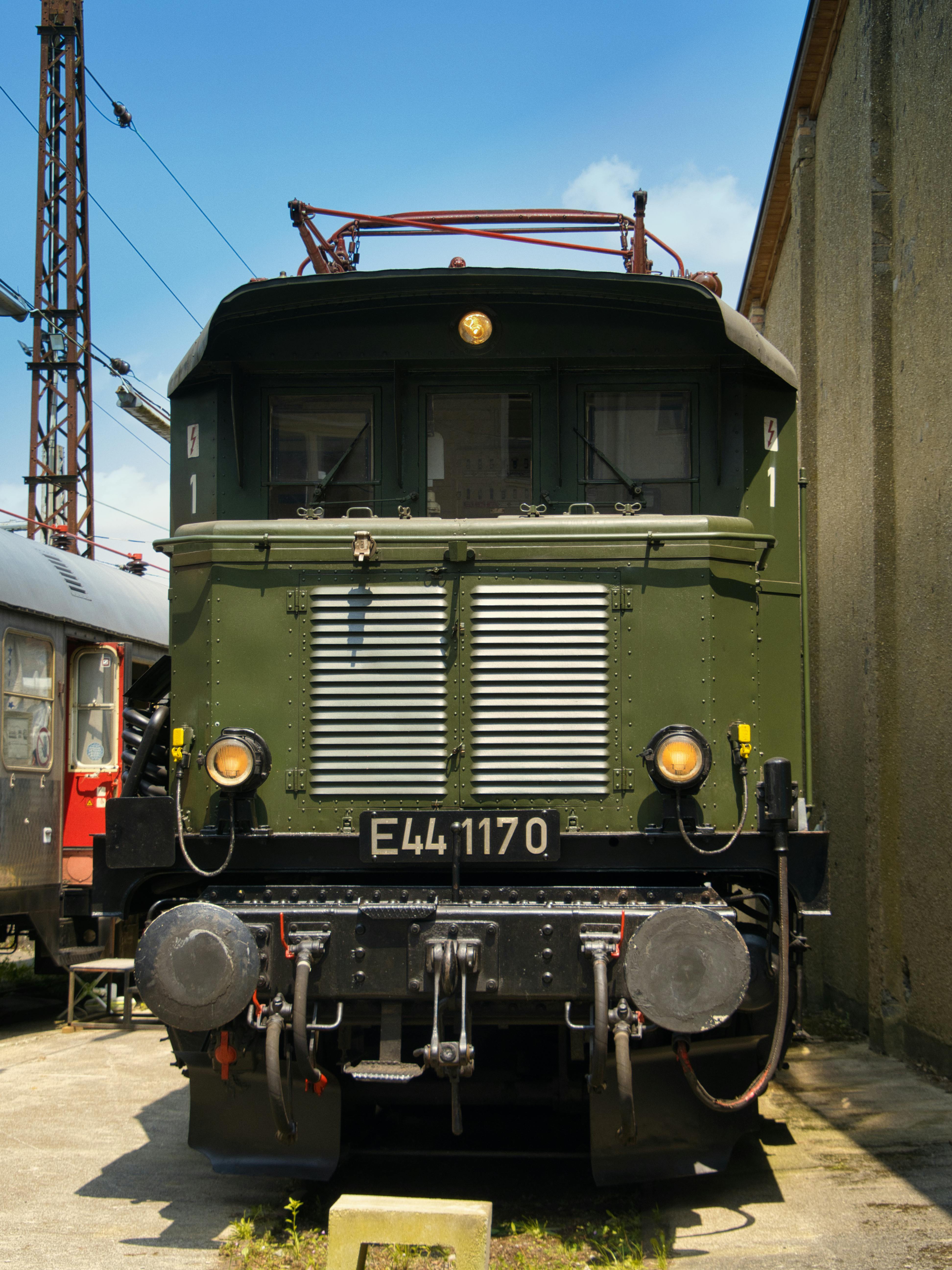 Front view of a vintage green train locomotive parked outdoors under bright sunlight.