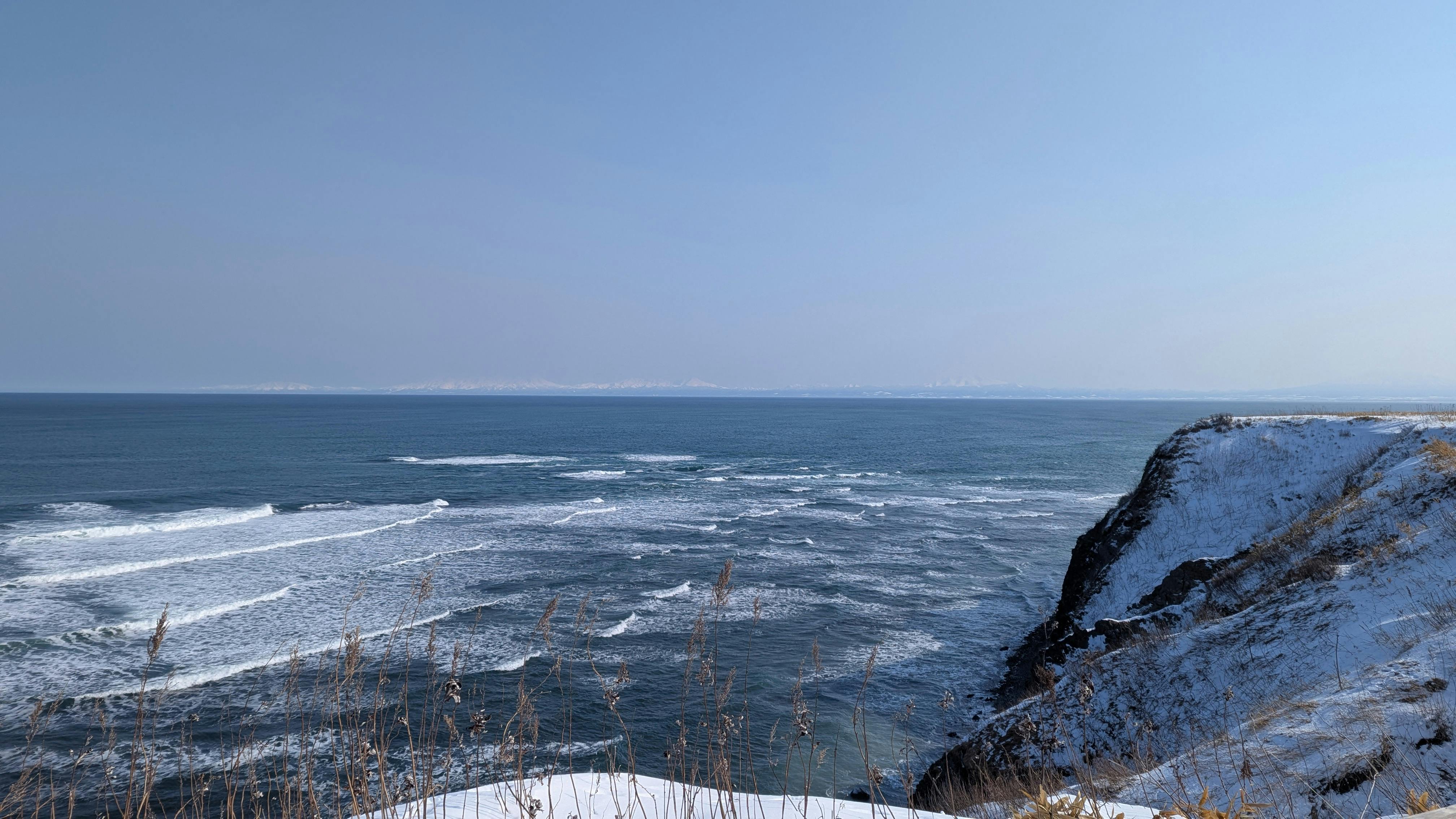 Scenic winter view of Cape Shiretoko with snow-covered cliffs and blue ocean waves.