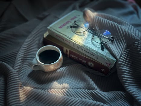 An inviting scene featuring books, glasses, and a cup of coffee on patterned fabric in soft morning light.