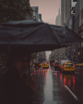 纽约市多雨的街道上，喜怒无常的城市场景中，出租车旁雨伞下人影模糊