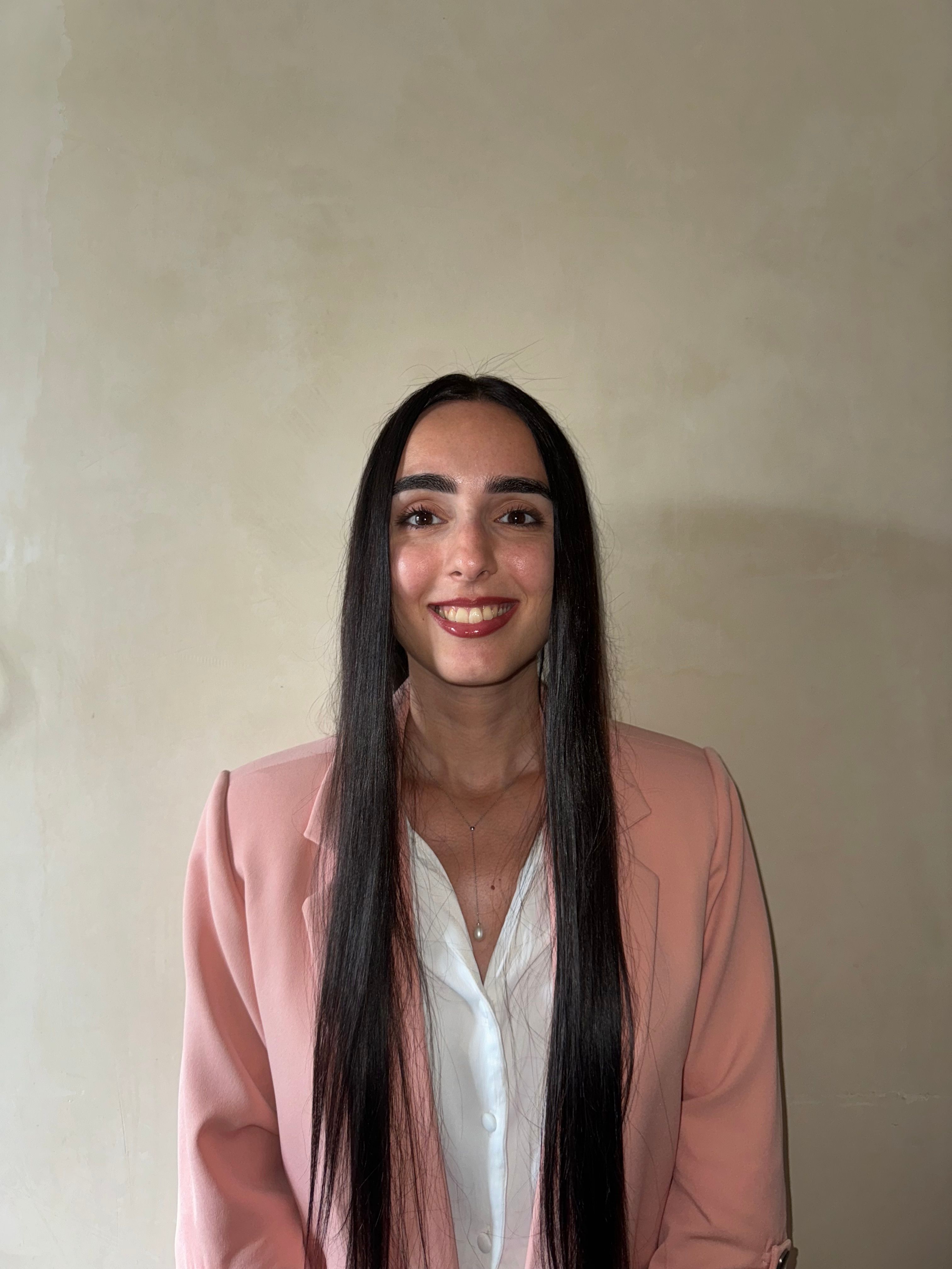 Portrait of a smiling woman wearing a pink blazer and white shirt indoors.