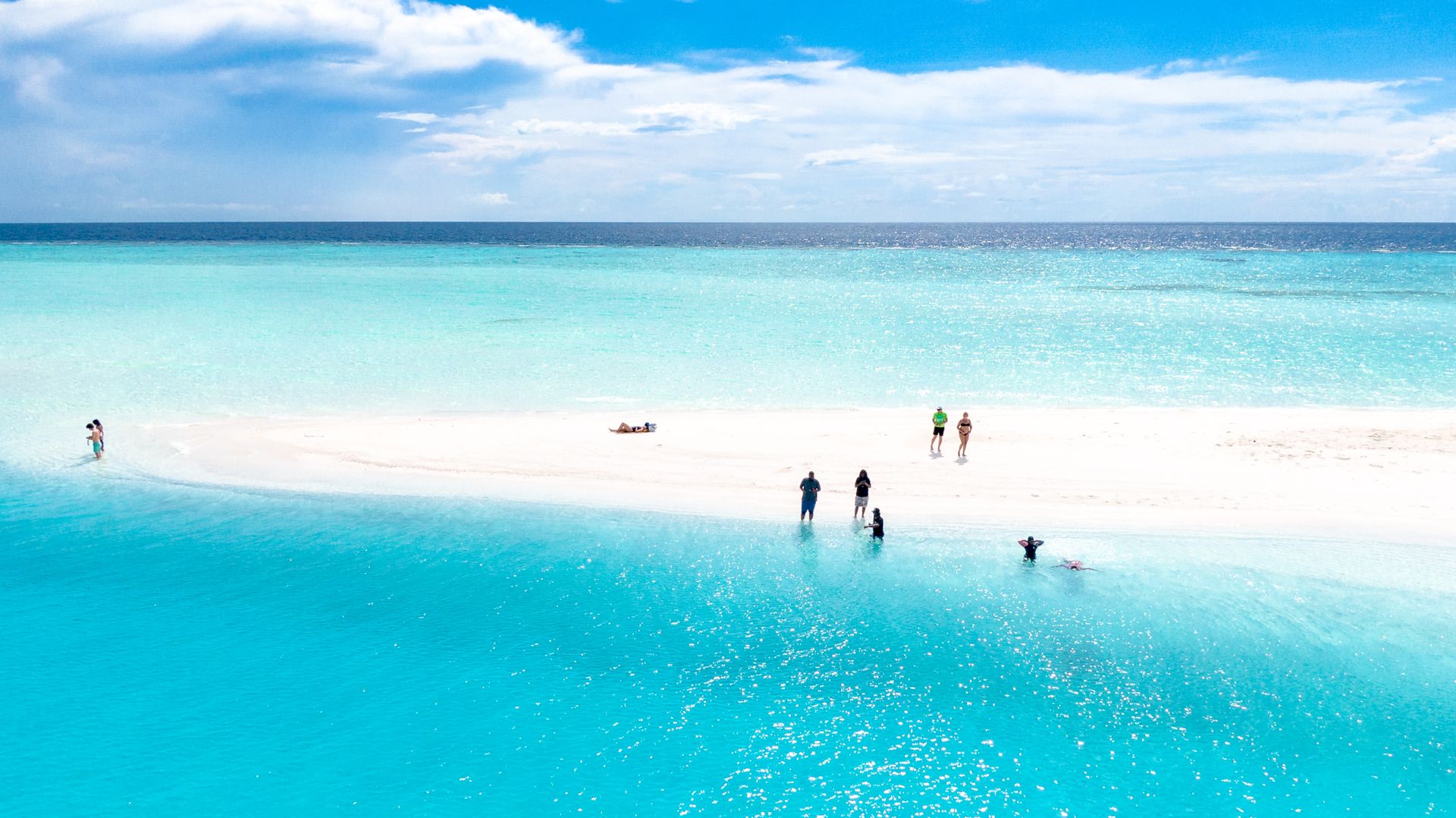 A stunning aerial view of a pristine beach in the Maldives with turquoise waters and people enjoying the sun.