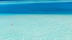 一张宁静的鸟瞰图，展现了一个人站在美丽海滩旁清澈碧绿的水中