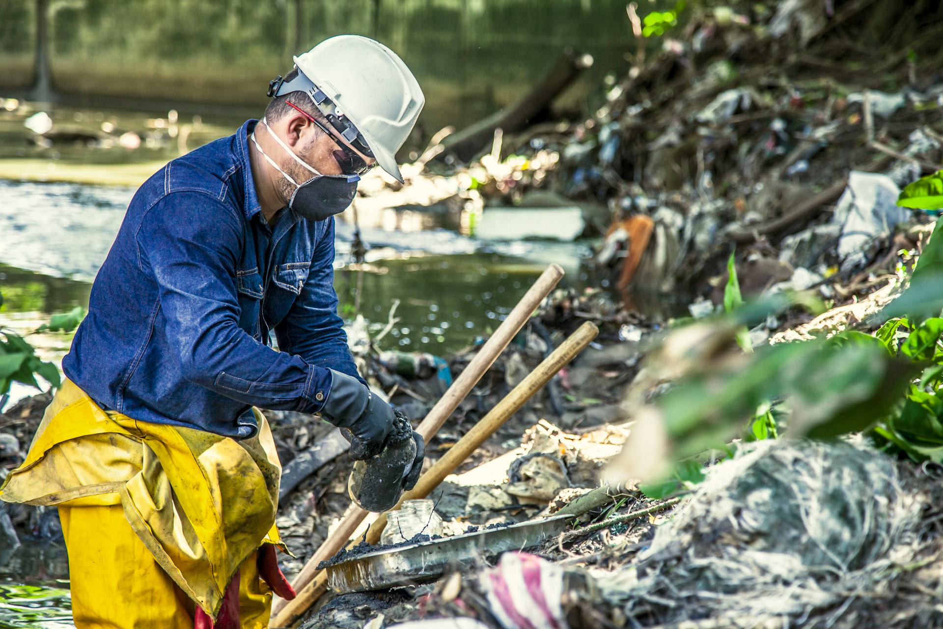 A worker in safety gear cleans polluted riverbanks, focusing on environmental protection.