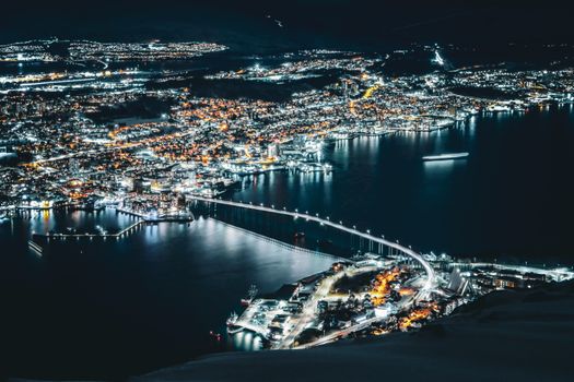 Breathtaking aerial shot of Tromsø, Norway cityscape with glowing lights reflecting on icy waters.