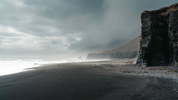 Moody seascape with black sand beach, cliffs, and dark clouds in Iceland.
