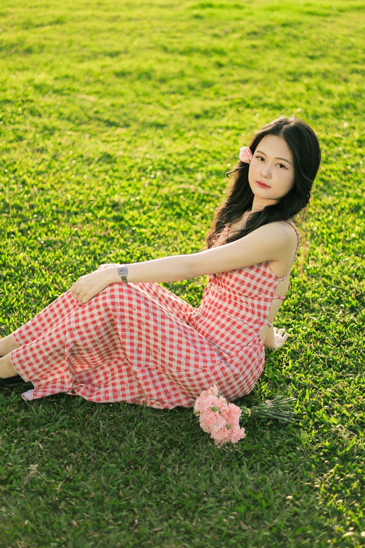 Woman in a red and white gingham dress sitting on green grass