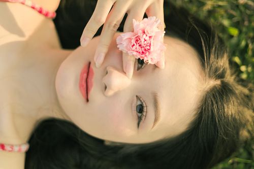 Free Close-up of a woman lying outdoors with a pink carnation flower, creating a serene and peaceful mood. Stock Photo