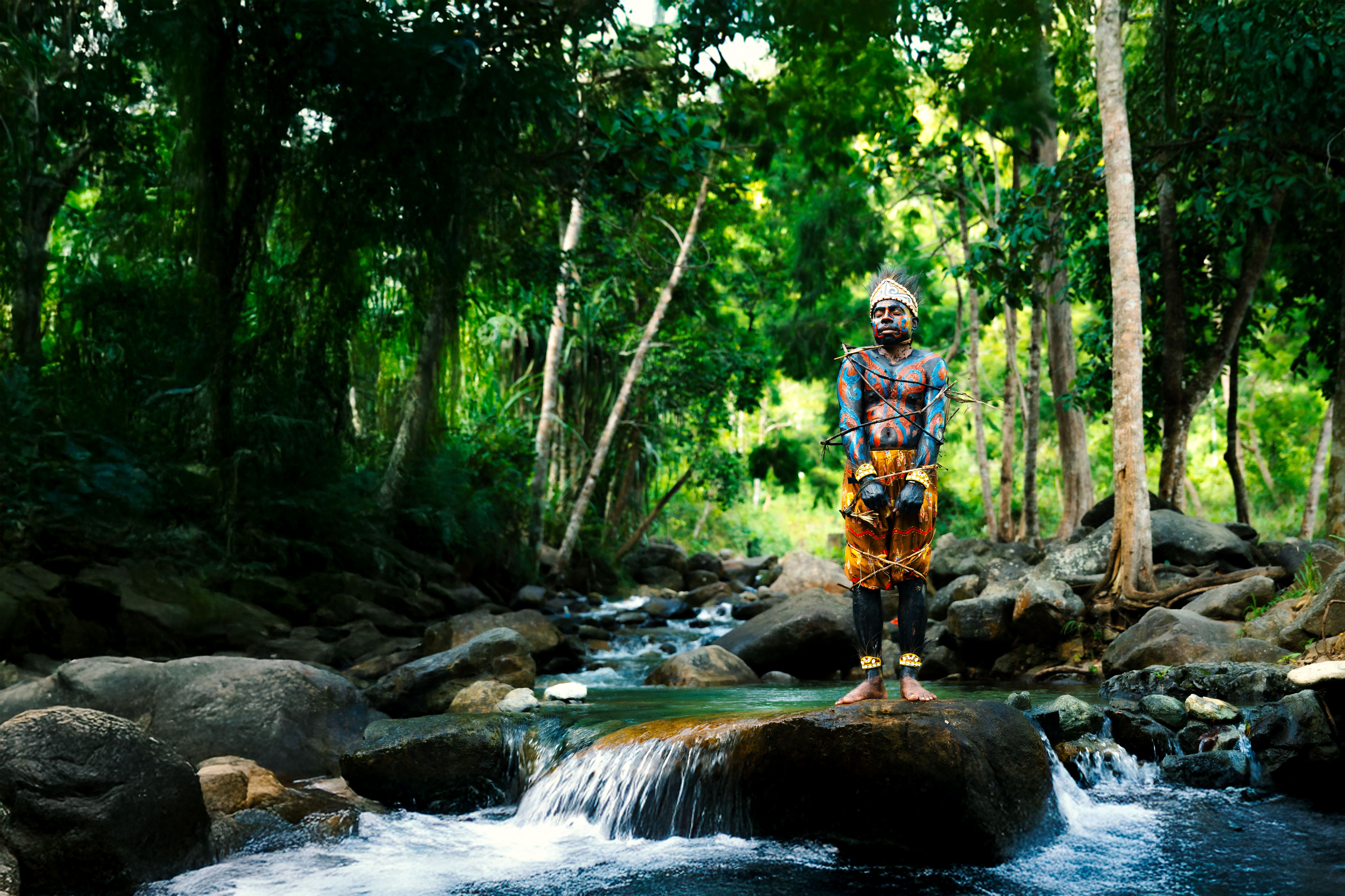 Person with traditional body paint standing on a rock in lush forest — iboga has been used ceremonially by the Bwiti peoples of Central Africa for centuries