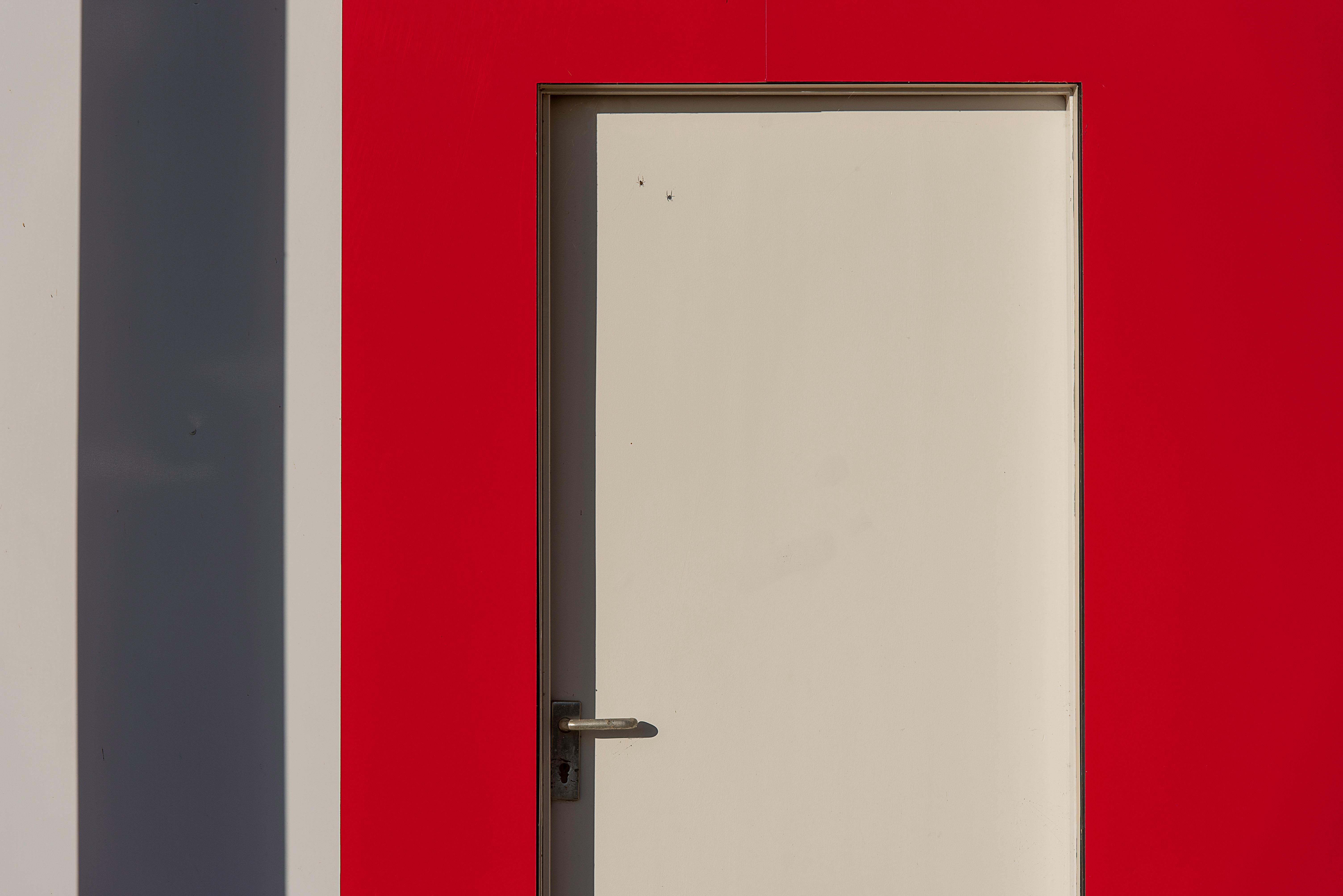 grátis Close-up de uma porta branca fechada contra uma parede vermelha com sombras e linhas limpas. Foto profissional