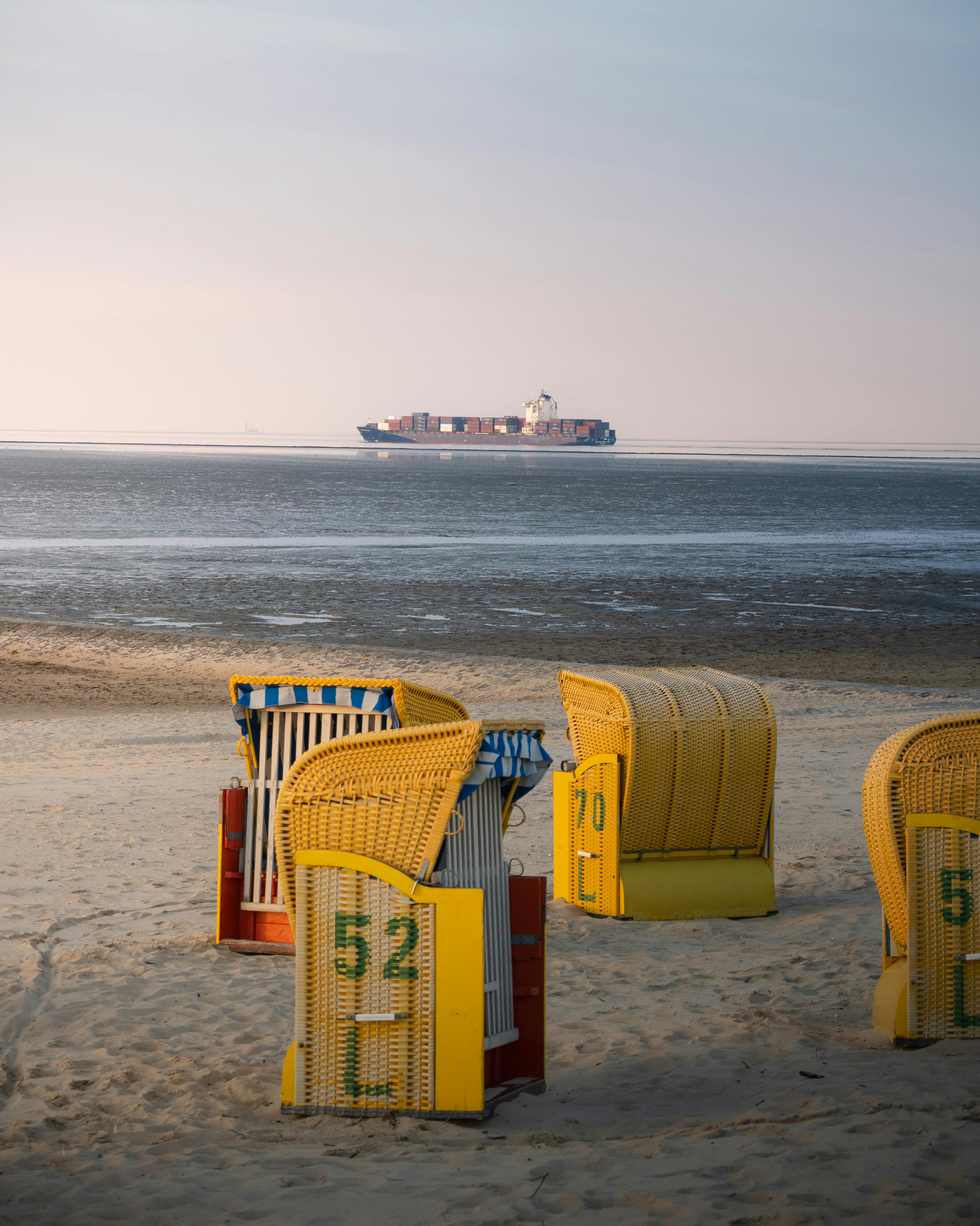 A tranquil beach scene in Cuxhaven, Germany, with beach chairs and a distant ship on the horizon.