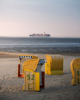 A tranquil beach scene in Cuxhaven, Germany, with beach chairs and a distant ship on the horizon.