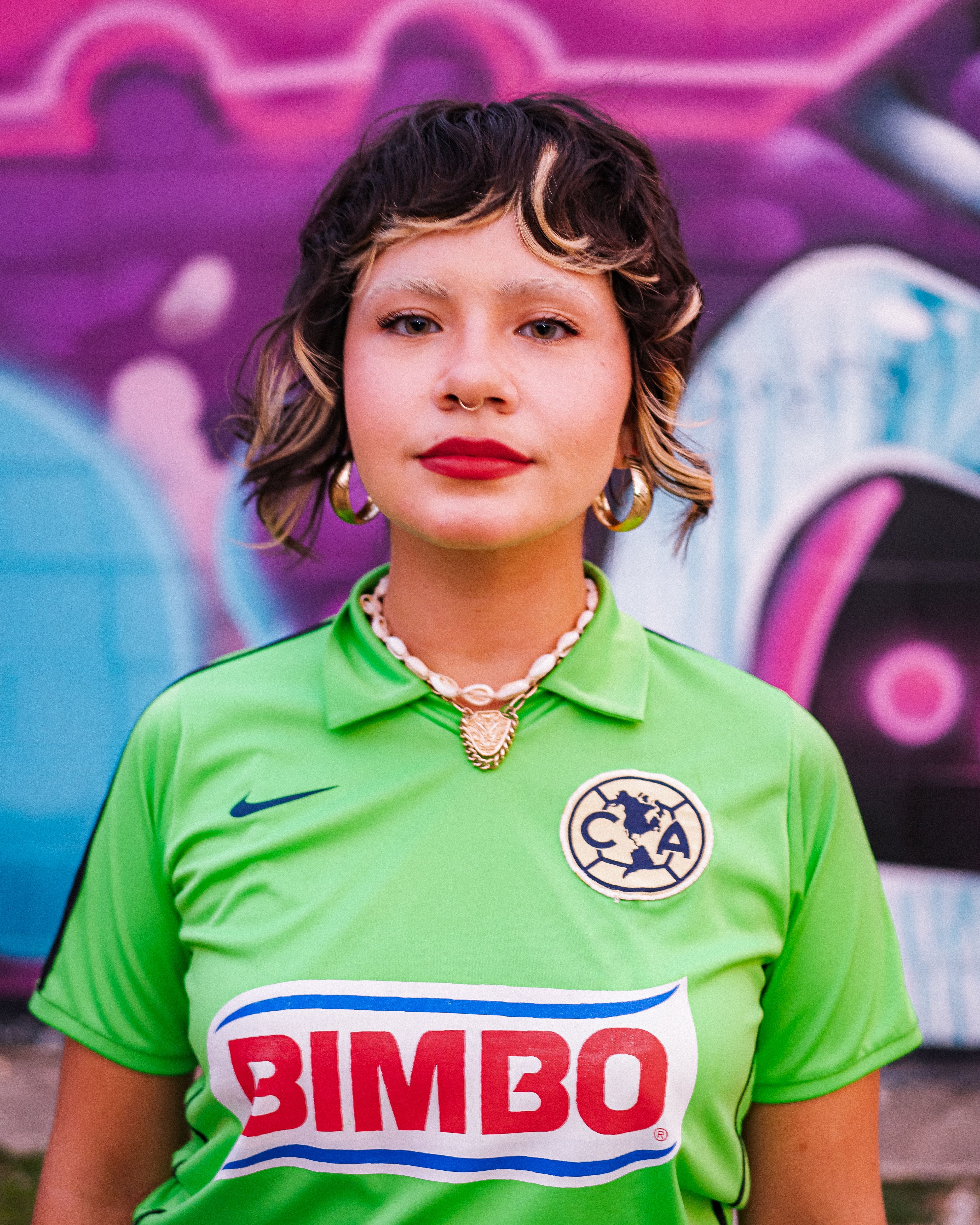 Stylish woman in vibrant soccer jersey poses against colorful graffiti backdrop.