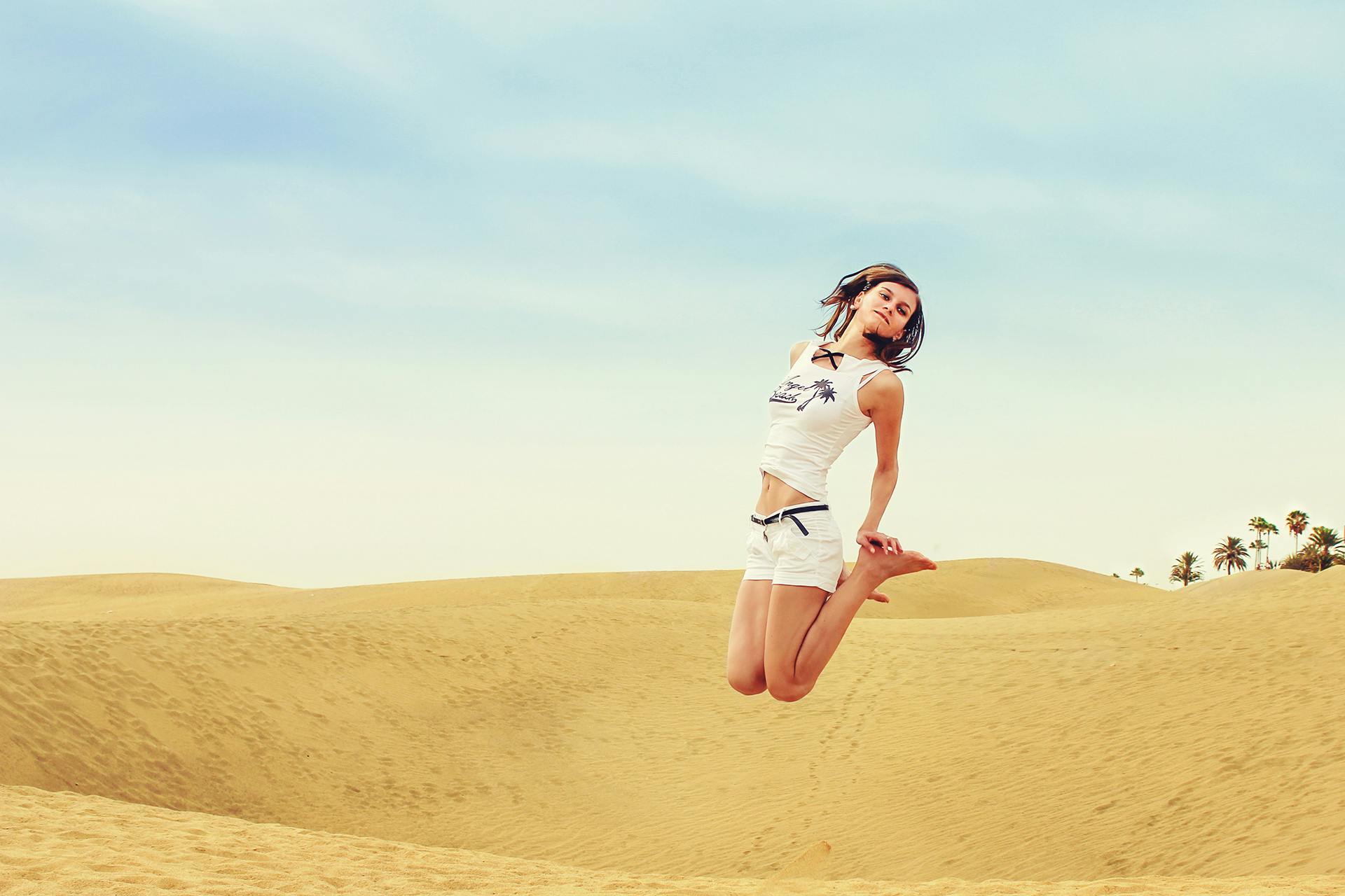 A cheerful woman jumps high in a sunny desert landscape, embracing freedom and adventure.