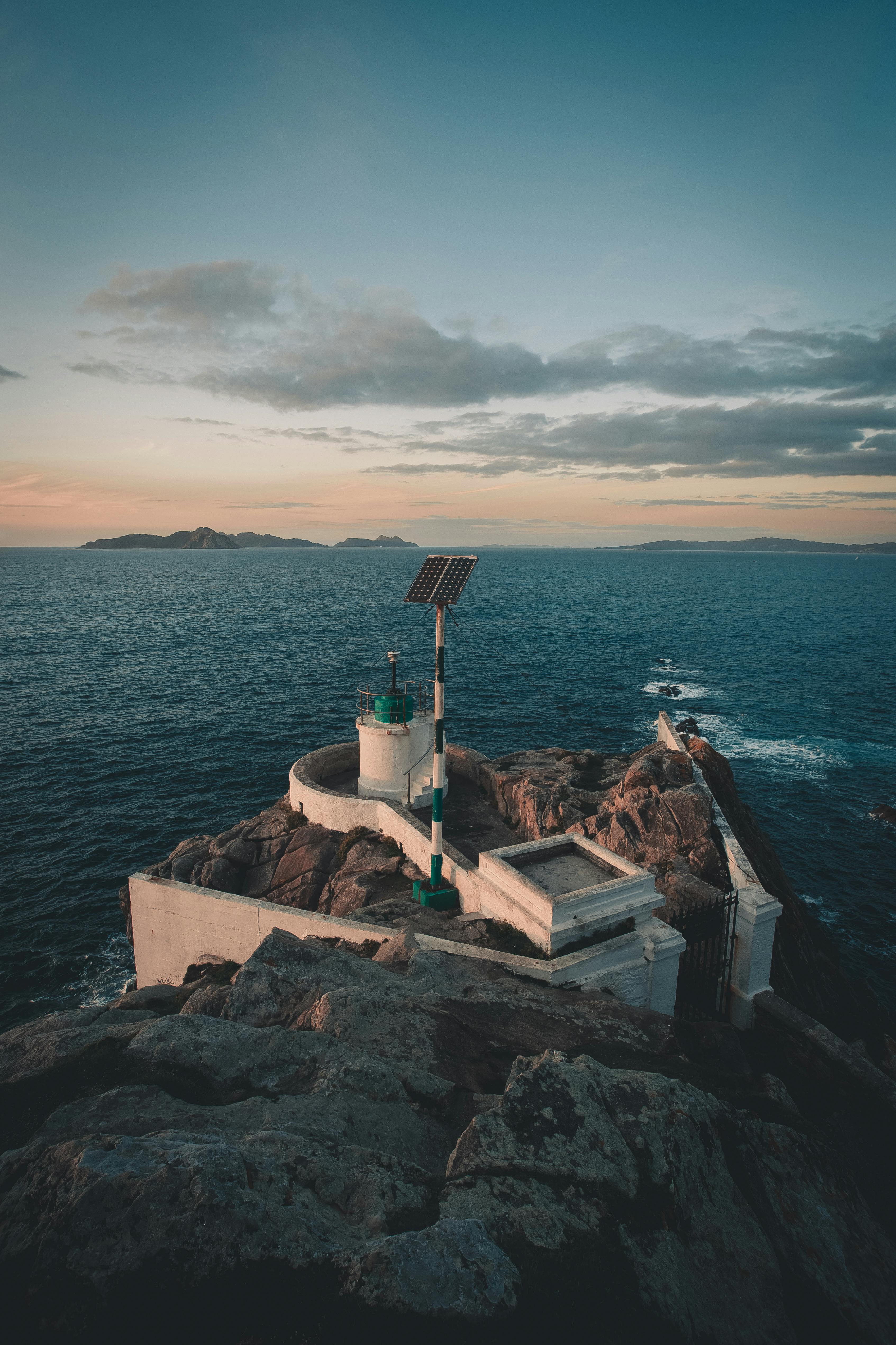 风景如画的灯塔坐落在岩石海岸上，日落时以戏剧性的海洋为背景