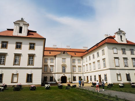 A grand historic European mansion with tourists exploring the grounds on a sunny day.