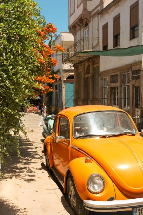 Free Classic orange car parked on a sunny street in Ayvalık, Türkiye, surrounded by historic architecture. Stock Photo