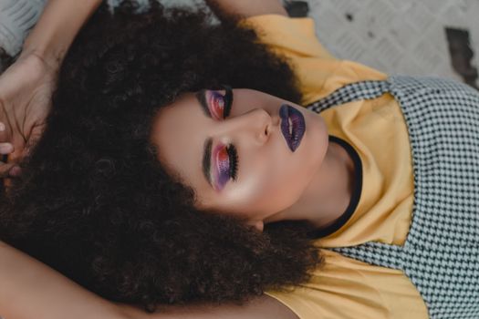 Portrait of a woman lying down with vibrant makeup and curly hair.