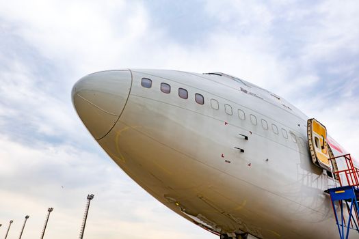 Detailed view of a commercial airplane's nose with an open hatch under a vibrant sky.