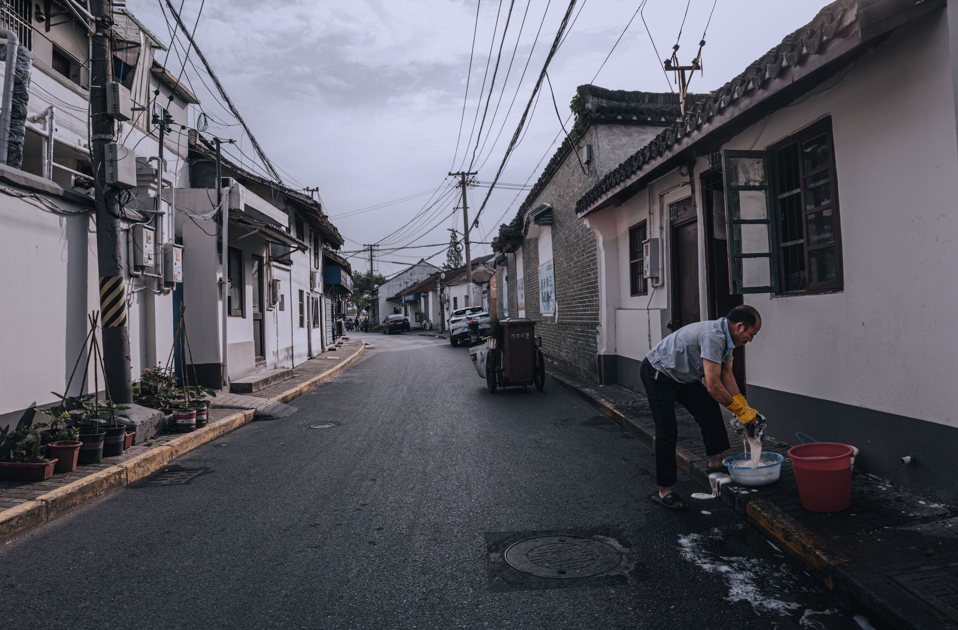 Man cleaning fish on a peaceful residential street in an East Asian neighborhood.