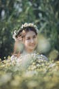 一位戴着精致花冠的女子微笑着，优雅地站在开满鲜花的田野中