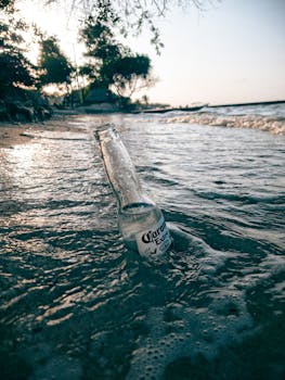 A solitary beer bottle rests on a Cartagena beach as dawn breaks, waves gently lapping the shore.