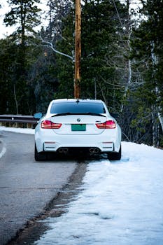 White sports car on a wintery road, surrounded by snow and trees, parked at roadside.
