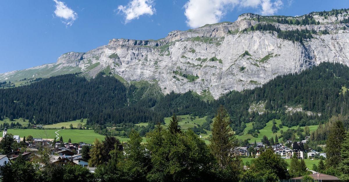 Stunning view of alpine village with majestic mountains and lush greenery under a bright blue sky.