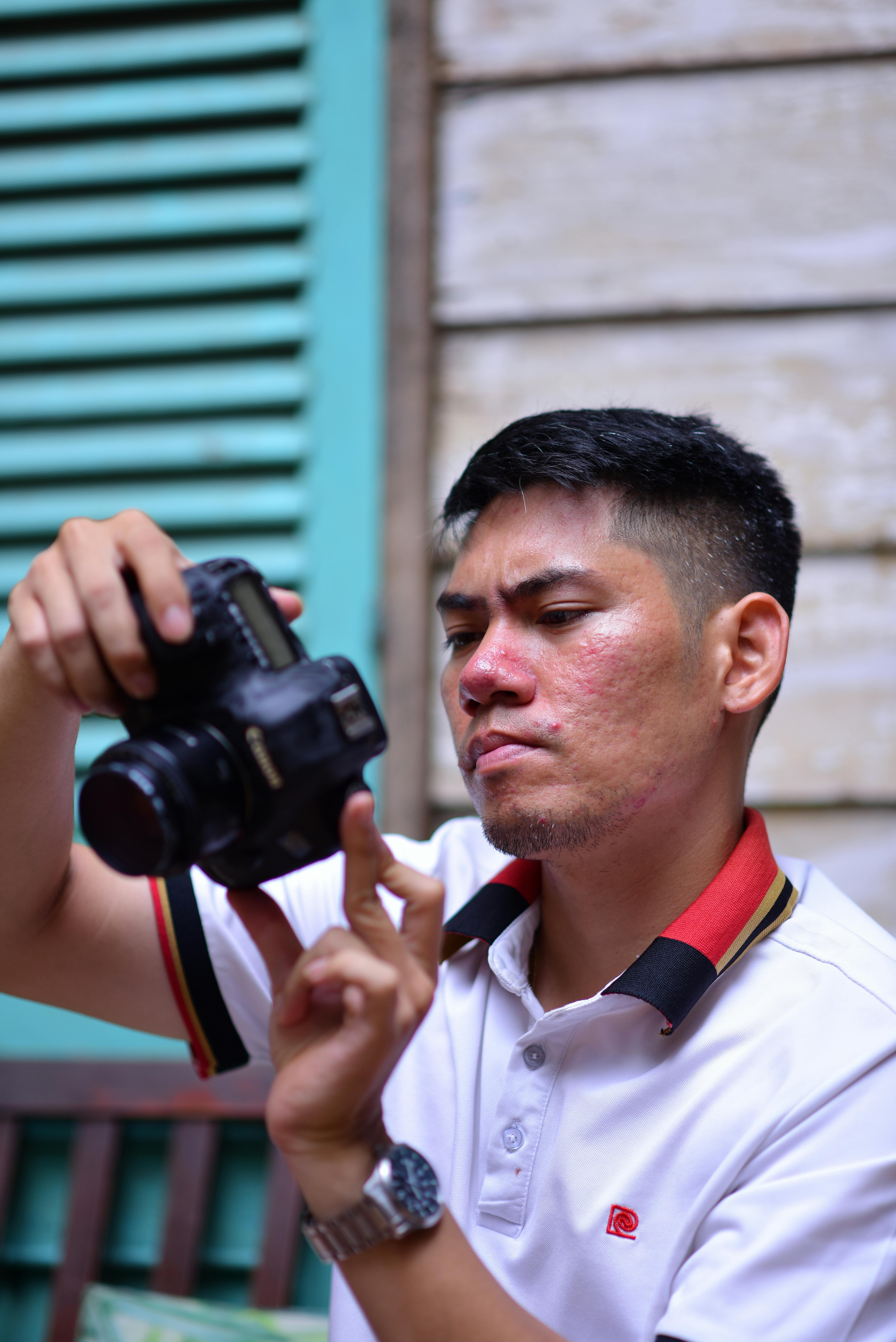 Young man adjusting camera settings in an indoor setting with a focus on technical detail.