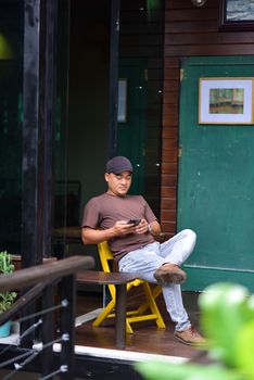 Man sitting comfortably on a yellow chair outdoors using his smartphone, enjoying leisure time.