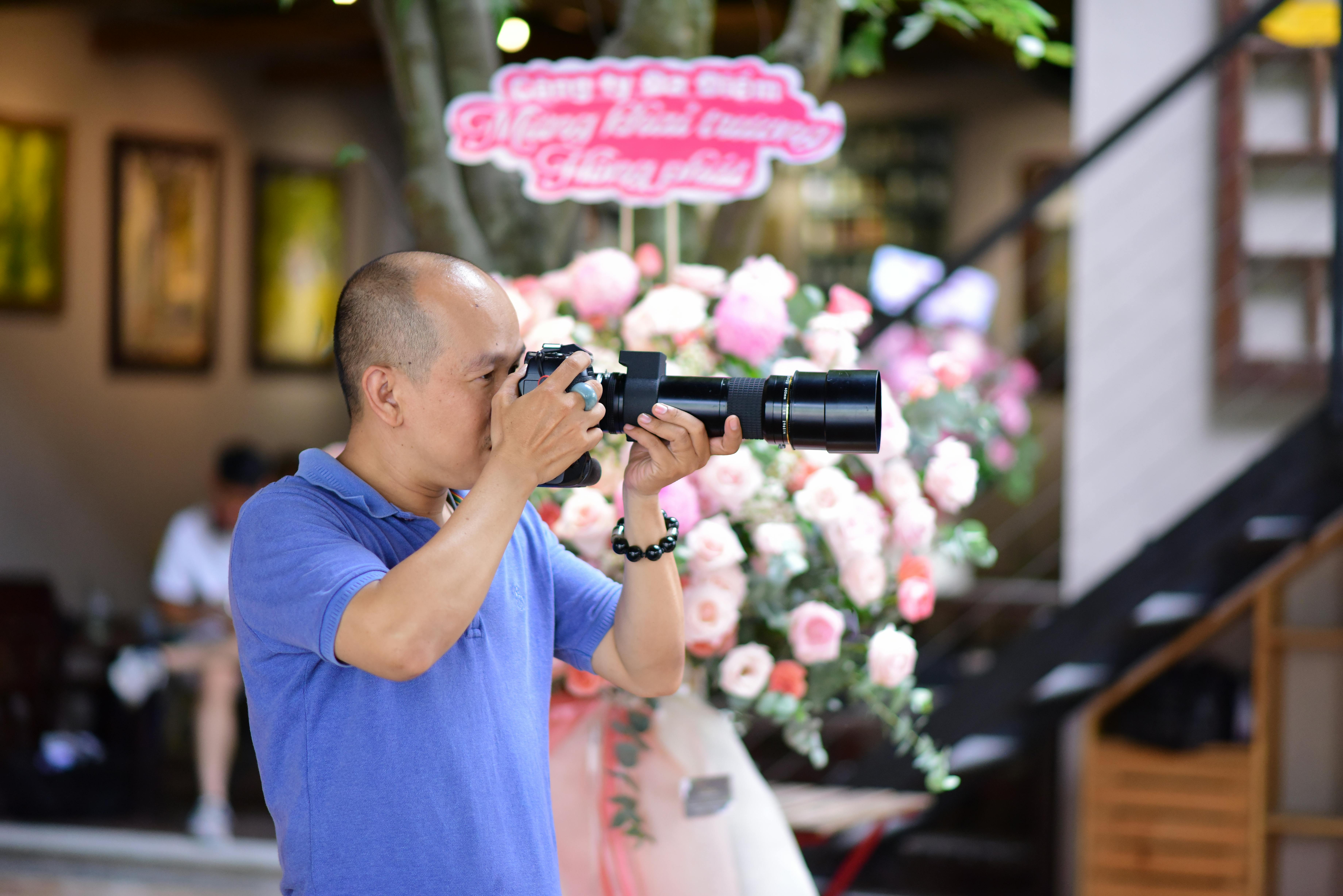 A man photographs a floral arrangement indoors, capturing the vibrant scene.