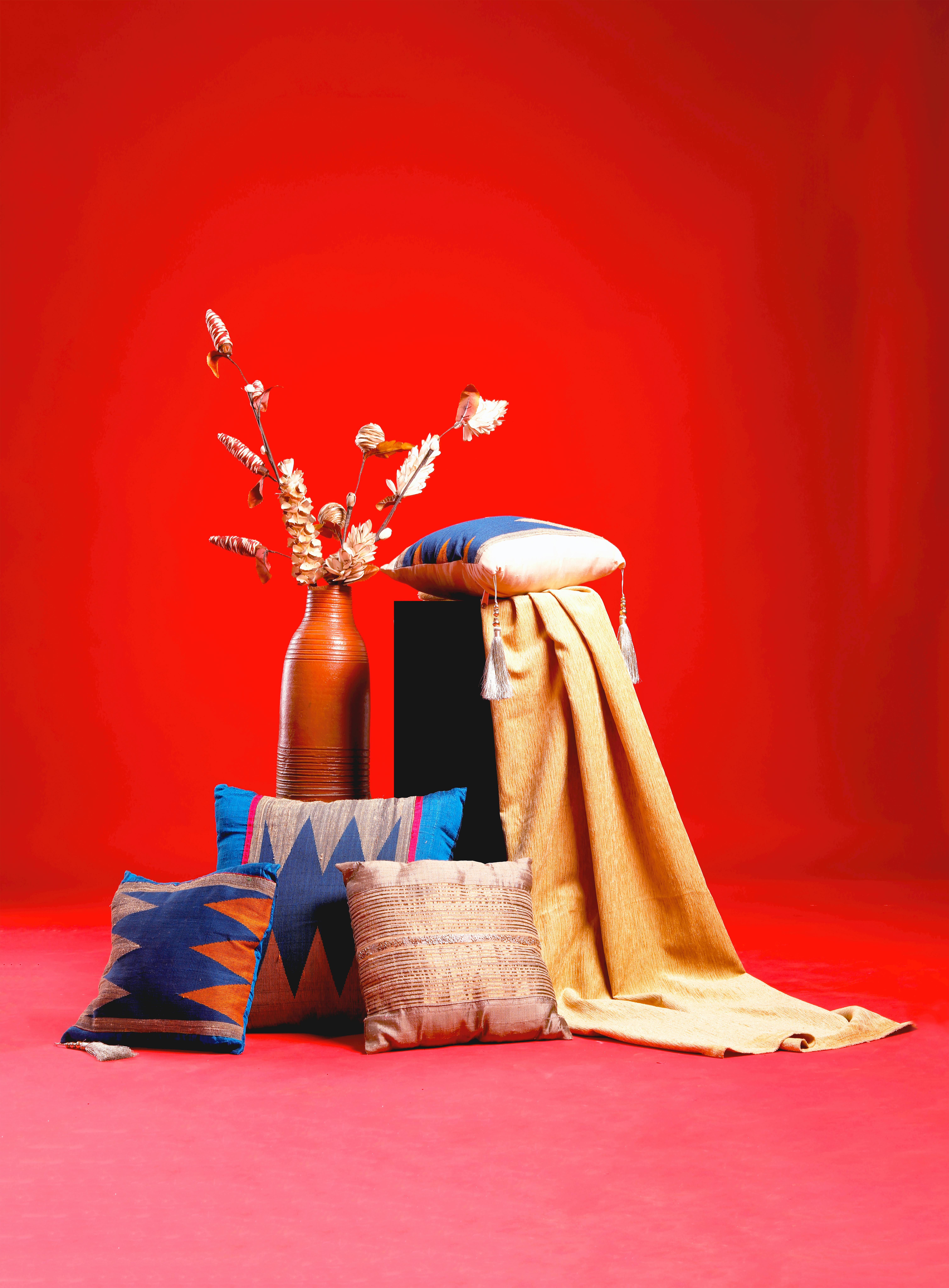 A bright arrangement of assorted textiles and a vase on a rich orange backdrop.